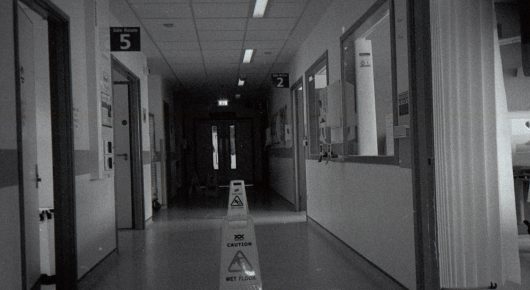 Still from Cambridge Connections: a black-and-white view down a long corridor with a wet-floor sign in the middle.
