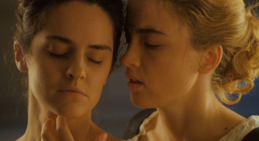 Still from Portrait of a Lady on Fire: a close view of two women's faces side by side in warm light, one with her eyes closed.