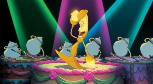 Still from Beauty and the Beast: an animated candelabra stands on a pink stage under green, purple and blue spotlights, with teapots and cups around him.