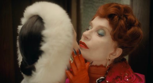 Still from The Blood Countess: a woman with red hair in a red dress, a white fur collar and orange gloves leans her head back with her eyes closed.