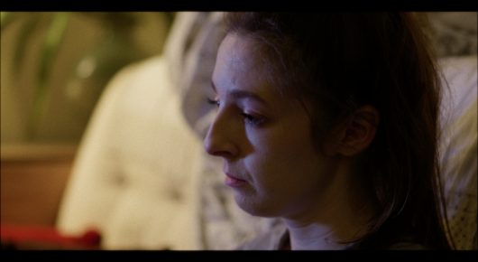 Still from Cambridge Connections: a close-up of a woman with curly hair looking down in warm light.