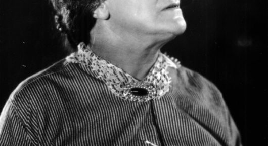 Black-and-white still from The Lodger: a close view of a woman in a striped dress with a beaded collar, her face turned upward and mostly out of frame.