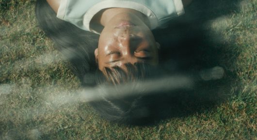 Still from Filipiñana: an upside-down close-up of a woman's face lying on the grass.