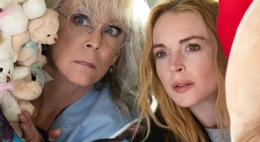 Still from Freakier Friday: a woman with grey-blonde hair and glasses and a woman with long strawberry-blonde hair lean together towards the camera, with soft toys beside them.