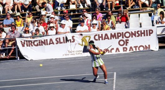 Photograph from Give Me the Ball: a tennis player prepares to hit a shot on court in front of a banner for the Virginia Slims Championship.