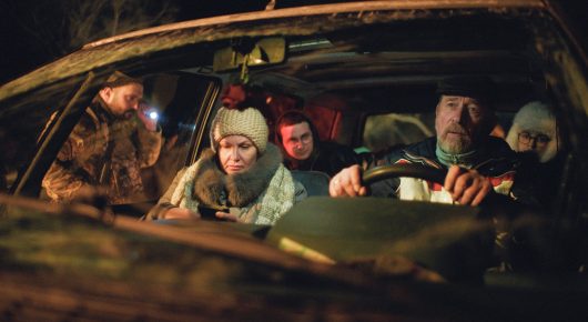 Still from I Rarely Wake Up Dreaming: several people in winter coats and hats sit packed into an old car at night, with a man at the wheel.