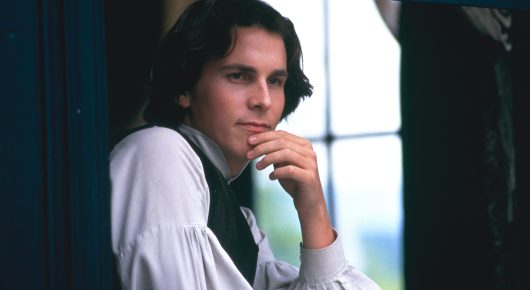 Still from Little Women: a young man with dark curly hair rests his chin on his hand beside a window.