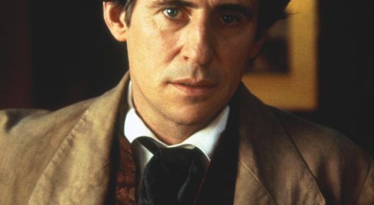 Still from Little Women: a close-up of a man in a brown coat and white shirt looking ahead with a serious expression.