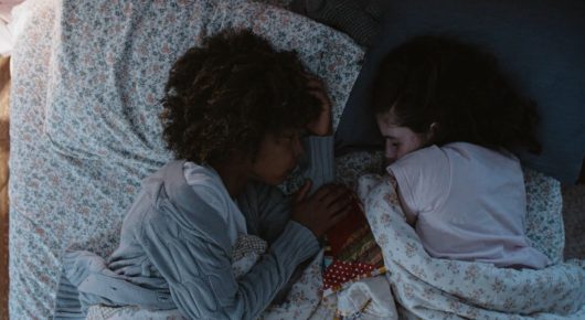 Still from Mouse: two children lie side by side in a bed with floral sheets.