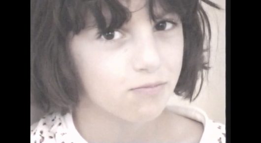 Still from My Father and Qaddafi: a close-up photograph of a young girl with a dark bob looking at the camera.
