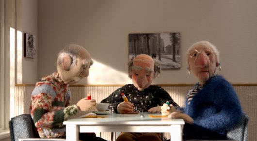 Still from Murmuration: stop-motion puppets of three elderly people sit around a white table in a dining room.