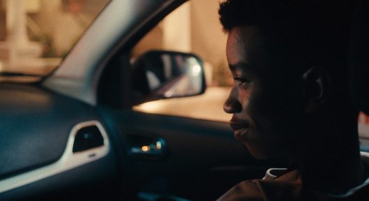 Still from One Last Night: a young man in profile sits in the passenger seat of a car, looking ahead.