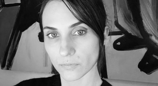 Black-and-white close-up of a woman with dark hair and a straight fringe looking directly at the camera.