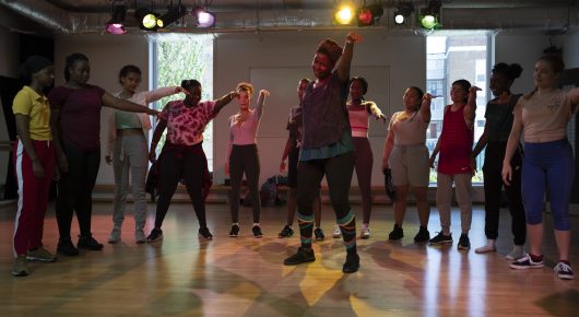 Still from Rocks: a group of girls dance together in a studio with spotlights, spread across the floor.
