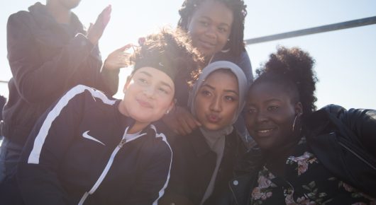 Still from Rocks: a group of girls squeeze together for a photo in bright sunlight.