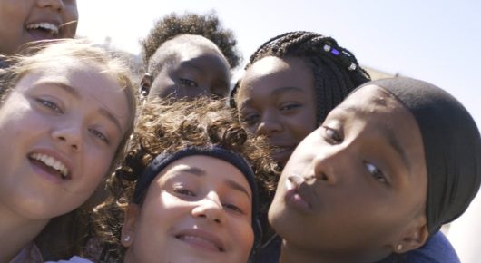Still from Rocks: a close-up selfie of several girls pressing their faces together and smiling.