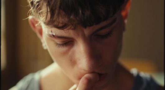 Still from Rage: a close-up of a young person with a fringe looking down with a hand held to their chin.