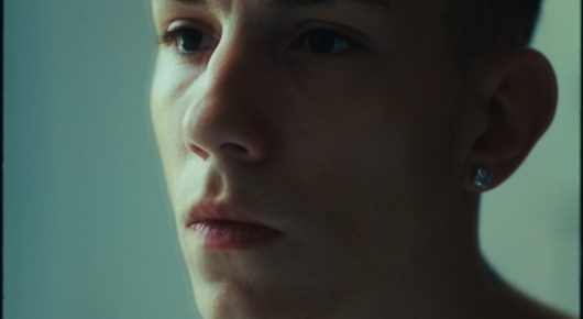 Still from Rage: a close-up of a young person's face in profile, lit in pale green.