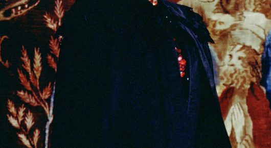 Still from The Secret Garden: a close view of embroidered red and gold leaf-patterned fabric beside a dark blue coat.