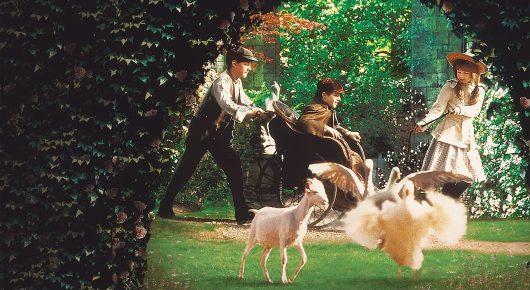 Still from The Secret Garden: children and animals, including goats and white geese, gather on a lawn in a garden.
