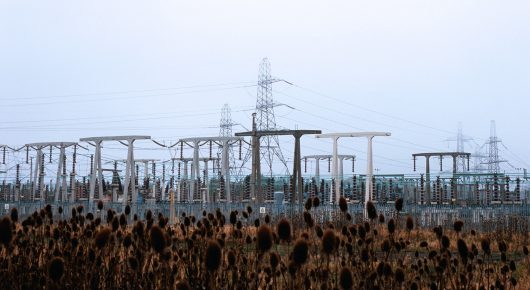 Still from The Selfish Giant: electricity pylons and a substation stand in a flat landscape of dry reeds under a pale sky.