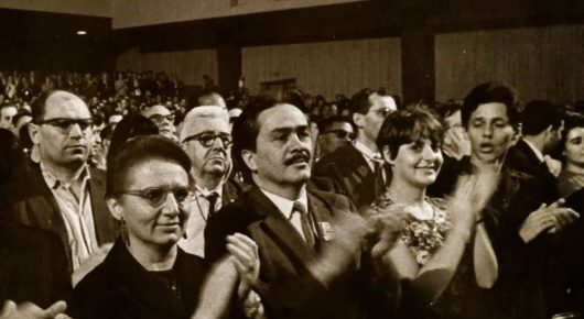 Still from Tricontinental: a black-and-white archive photograph of delegates in suits applauding in a conference hall.