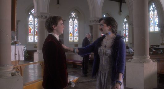 Still from Cambridge Connections: a man in a dark jacket and a woman in a blue cardigan hold hands in a church aisle.