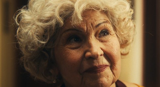 Still from The Last Ingredient: a close-up of a smiling older woman with curly white-blonde hair.