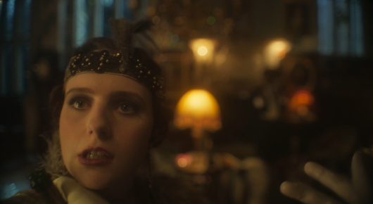 Still from The Painting and The Statue: a close-up of a young woman with a beaded headband in a warmly lit room with lamps.