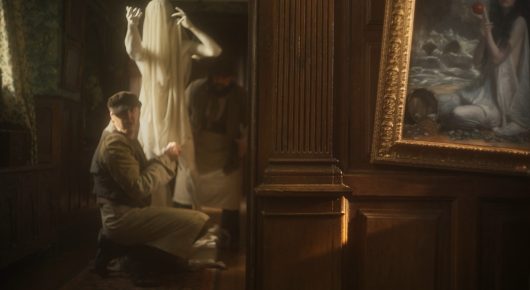 Still from The Painting and The Statue: a person crouches beside a pale statue in a dim, gold-toned room with a large framed painting on the wall.