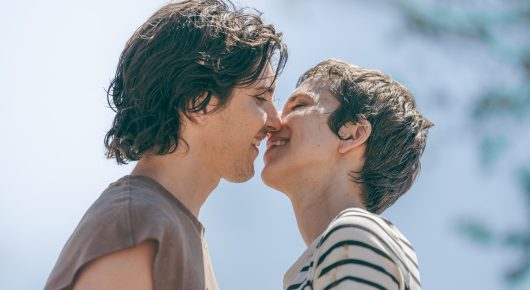 Still from Viva: two young people kiss outdoors against a pale sky.