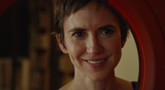 Still from Viva: a woman with short brown hair smiles, framed by a round red opening.