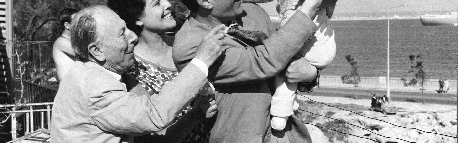 Still from El Verdugo: a black-and-white photograph of a family group outdoors, a man lifting a child while others stand close, with the sea behind them.