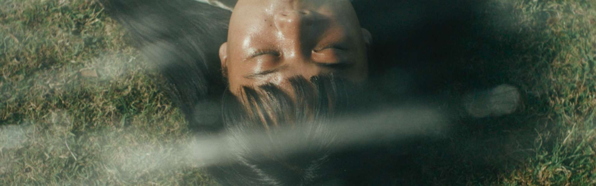 Still from Filipiñana: an upside-down close-up of a woman's face lying on the grass.