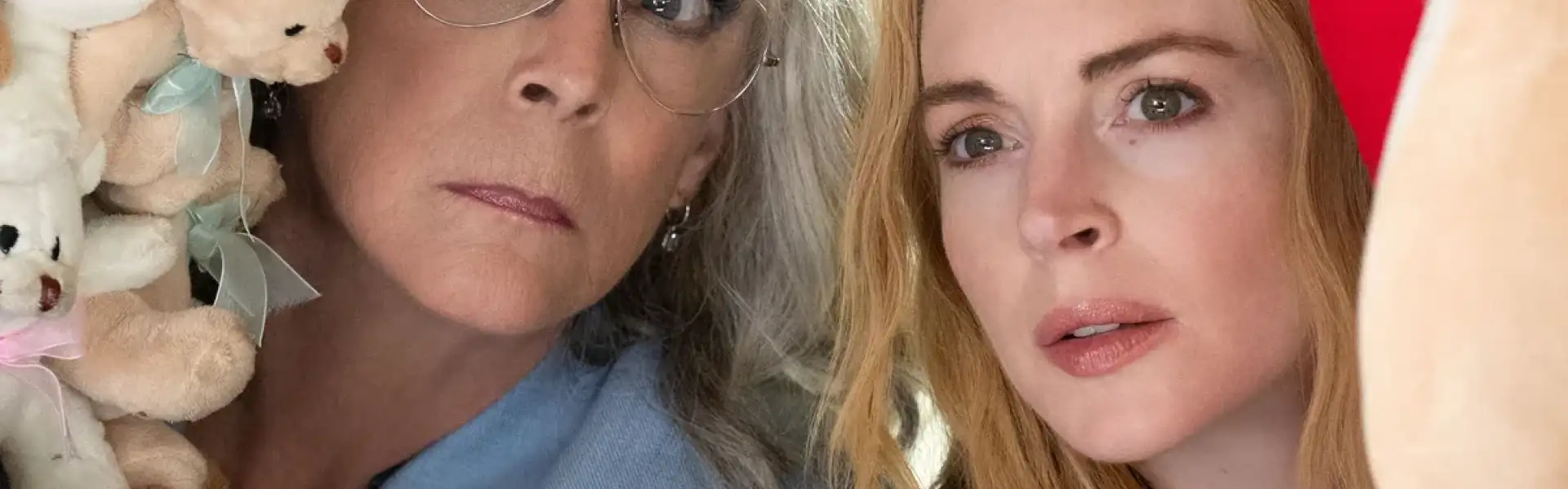 Still from Freakier Friday: a woman with grey-blonde hair and glasses and a woman with long strawberry-blonde hair lean together towards the camera, with soft toys beside them.