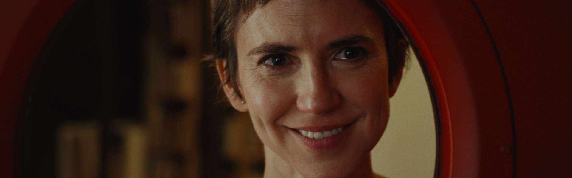Still from Viva: a woman with short brown hair smiles, framed by a round red opening.