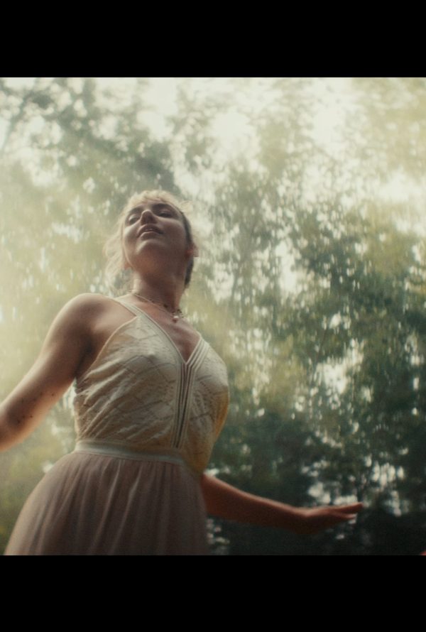Still from Todd and The Toad: a woman in a pale dress stands with her arms outstretched in a sunlit forest.